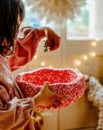 Child holding a red and white patterned stepping stone with a blurred indoor background