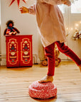 Child playing with a red and white blush limited edition original on a wooden floor, surrounded by toys and decorations.