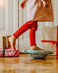 Child in red pants stepping on stepping stones with wrapped gifts on the floor