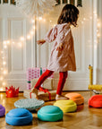 Child playing with colorful stools in a room decorated with string lights